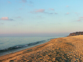 A captivating view of the seashore in Calabria at sunset, where golden sunlight gently illuminates...
