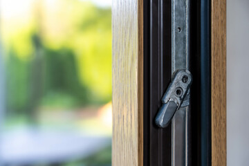 Window tilt-and-turn metal latch mechanism on wooden frame, close-up detail with daylight outdoor...