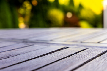 Close-up view of wooden garden table planks with blurred summer greenery in background, captured in afternoon light, useful for product placement or outdoor setting concepts