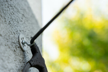 Cable mount detail on wall with power tool wire attached in outdoor setting with defocused green background, concept of home improvement and utility