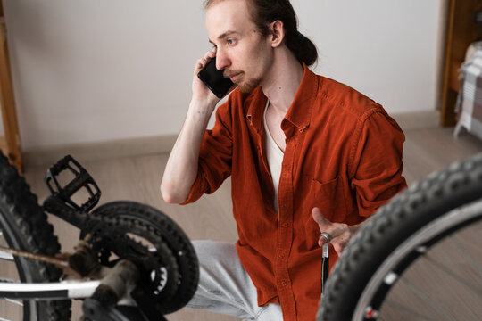 Young long-haired man calling mechanic to discuss fix bicycle breakdown