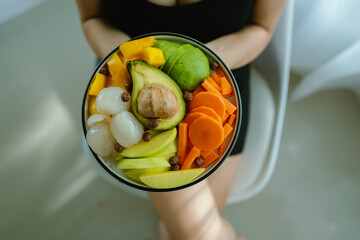 A woman enjoys a fresh, healthy salad made with organic vegetables at home, promoting a balanced...