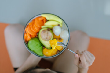 A woman enjoys a fresh, healthy salad made with organic vegetables at home, promoting a balanced...