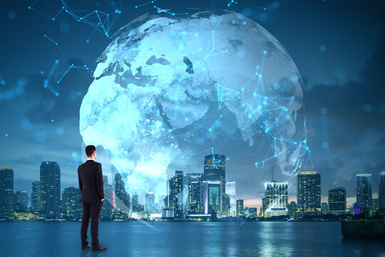 Businessman looking at digital world map with global network connections over modern city skyline at night, symbolizing internet and technology.
