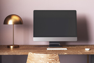 Modern desktop computer with blank screen on wooden table in cozy home office with lamp and chair...