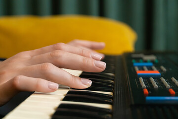 Close-up of female hands playing a synthesizer, creating music in a cozy home or professional...