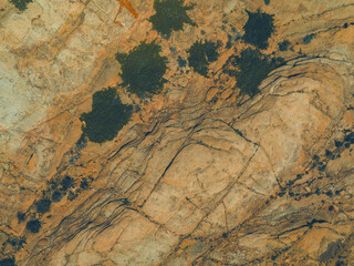 Aerial top view photo of reddish volcanic mountains with scattered green bushes and rugged rocky terrain under natural daylight.