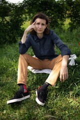 Young man rests thoughtfully on grass in a serene outdoor setting during a sunny afternoon