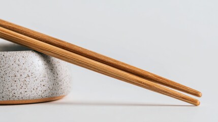 Elegant wooden chopsticks gracefully resting on a minimalist ceramic holder against a serene white background