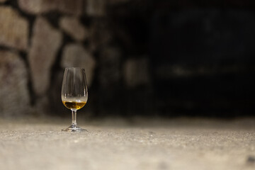Glass of aged wine in a stone wine cellar with soft light, showing the calm and authentic...