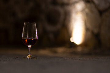Glass of aged wine in a stone wine cellar, capturing the quiet, authentic atmosphere of traditional wine tasting and maturation.