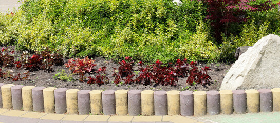 A flowerbed with colorful plants – green bushes and red flowers – is enclosed by a decorative...