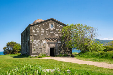 Yason church in Ordu city. Historic stone building set against a backdrop of lush greenery and a serene shoreline. For themes related to history and religion.