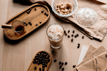 Iced coffee in a clear glass with a rustic setup. Coffee beans, brown sugar, and warm light add cozy vibes.