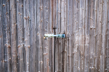 An aged wooden door with rustic metal hinges and deep weathered texture. Old wooden door with lock.