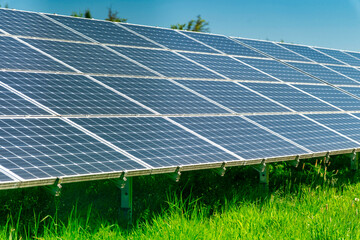 Solar panels farm under a bright blue sky surrounded by green meadows.