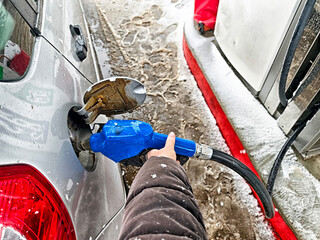 Filling up a silver car with fuel during a snowy winter day at a gas station