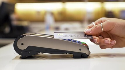 An adult female's hand processes a payment by inserting a credit card into a modern POS terminal, representing a convenient financial transaction at an indoor retail point. - Powered by Adobe