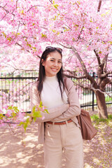 Asian woman smiling under blooming cherry blossom tree in springtime