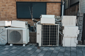 Stack of discarded air conditioner units and parts beside urban building