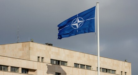 NATO flag waving in front of modern building under cloudy sky  