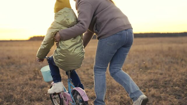 childhood dream. mother helps child learn ride bike. son pedals two-wheeled bicycle.baby riding lesson. childhood dream ride bike. caring young mother travels with her daughter in the park evening.
