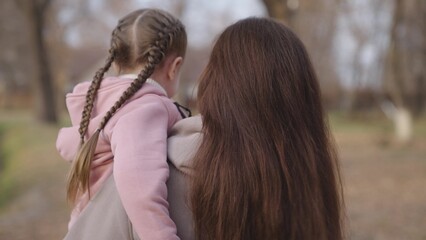 Fototapeta premium mom carries a little child in her arms, the kid got tired and climbed into his mother's arms, a walk with a baby in a city park, the life of motherhood, a beloved daughter in a happy family.
