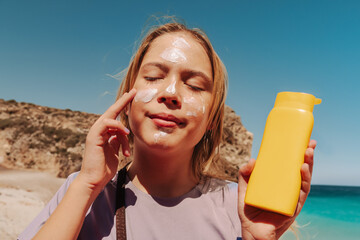 Teen applying sunscreen on face, arm, and leg under direct sun. Summer skincare, blue sky, beach background, and beige hammock. Sun protection routine, outdoor wellness