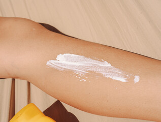 Teen applying sunscreen on face, arm, and leg under direct sun. Summer skincare, blue sky, beach background, and beige hammock. Sun protection routine, outdoor wellness