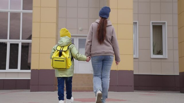 affectionate mother leads the child back to school, to teach first lessons of childhood, a school student goes hand in hand with mom, happy family, a cheerful boy son with mom go to school building.