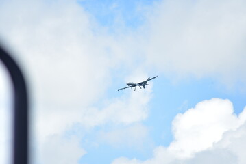 An aircraft soaring high in the sky, captured against a cloudy blue backdrop.