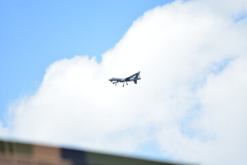 A drone flies in a blue sky with white clouds, viewed from a low angle.