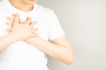 Young female suffering from chest pain over gray background. Causes of chest pain incluede angina,...