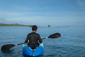 A man paddles a kayak on a tropical island. Aman enjoying a sunny day while kayaking. Low angle shot