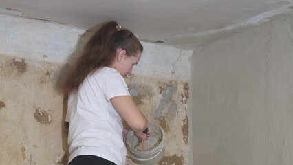 woman plasterer plasters the wall with brush, renovation work of an apartment, industrial...