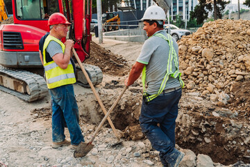 Construction workers repairing city infrastructure with heavy equipment and red polypropylene pipes. Urban utility maintenance, excavation, and roadwork in progress