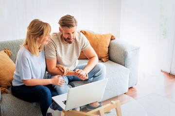 Married couple sitting on sofa and using laptop computer