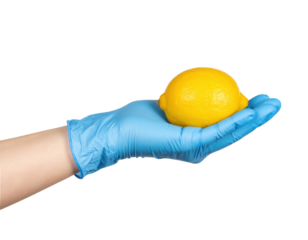 A hand wearing a blue medical glove is holding a fresh, bright yellow lemon.