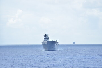 A large military transport ship sails on a calm ocean, with smaller vessels visible in the distance.