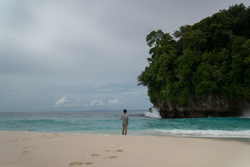 A man fishes off the coast of a tropical island. An angler carries a fishing rod on the shore in turquoise water