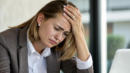 Stressed businesswoman holding head in frustration while working on laptop in office, struggling with challenging work tasks