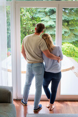 Rear view of a couple standing at the patio door and looking out of the window
