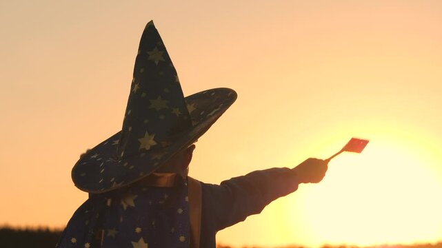 boy in a hat conjures magic wand at sunset, halluin, believe in children's magic, kid plays in the glare of the sun, child's carnival costume for holiday, an astranom festive outfit, childhood dream.