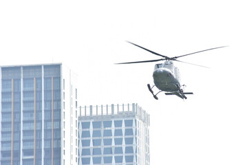 A light gray helicopter flies over modern city buildings against a plain white sky. © Sony