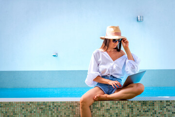 A woman sitting on the edge of the pool using a laptop