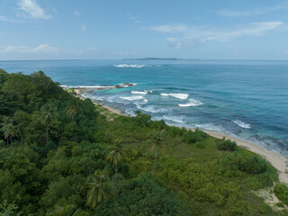 An aerial view of a tropical island with white sand beaches and turquoise waters. Waves crashing on a white sandy tropical beach