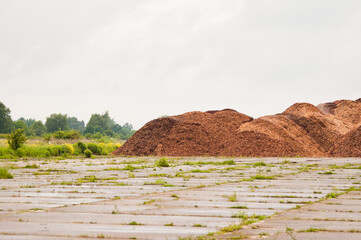 Mountains of wood chips close up, in the background a meadow, forest and gray sky
