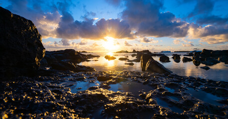Panoramic view of north coast near Anse la Raie on Mauritius island with idyllic sunrise atmophere and colorful sky. Silhouettes of volcanic black rocks at low tide. Paradisiacal  vacation destination
