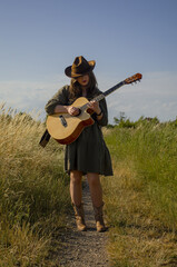 A girl with a guitar in cowboy style. Cowboy hat and boots. Sunny atmospheric photos.