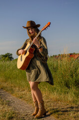 A girl with a guitar in cowboy style. Cowboy hat and boots. Sunny atmospheric photos.